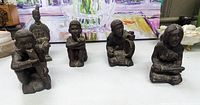 Group of five dark soapstone tribal figures arranged on a tabletop, showing various poses and details.