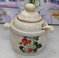Front view of cream-colored ceramic soup tureen with matching lid and ladle, decorated with strawberry and flower painted design.