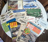 Top-down view showing an assortment of vintage Chevrolet manuals, brochures, and automotive magazines spread out on a white table.