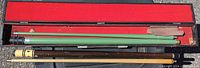 Four vintage pool cues displayed inside a brown carrying case lined with red felt.