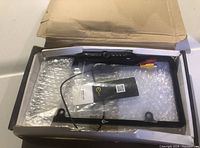 Rear-view camera mounted on a black license plate frame in a partially opened box with bubble wrap.