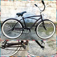 Side view of the brown beach cruiser bicycle showing the full frame, white wall tires, chain, pedals, and handlebars against a concrete wall.