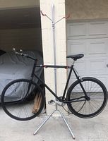 Full view of the gravity pole bike rack stand holding a bike by the frame with red hooks and tripod base in garage setting.
