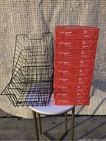 Nine reams of Staples copy paper stacked vertically showing side label with paper specifications and brand logo, next to three black metal wire baskets on a small table.