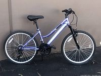 Side view of purple Huffy girls mountain bike showing frame, saddle, tires, and handlebars.