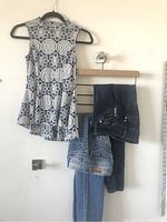 Sleeveless top and two pairs of jeans hanging on hangers against wall, showing all three items in the lot.