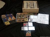 Top-down image showing a storage box filled with rows of baseball cards, along with sheets and small groups of cards laid out on a black surface.