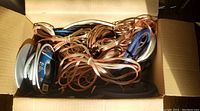 Box filled with assorted spools and loose cables including speaker wire, audio cables in various colors and types.