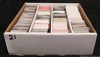 Cardboard storage box with multiple sections filled with trading cards, showing card backs and organized rows