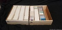 Two white cardboard storage boxes filled with numerous trading cards, some sleeved and some loose.