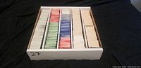 First image shows a cardboard storage box containing thousands of assorted trading cards separated by color sleeves: white, pink, green, red, blue.