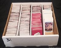 Box with four large stacks of assorted trading cards sorted with cardboard dividers. Cards show different edges and colors indicating variety in the collection.