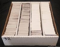Photo of a white storage box divided into four sections, each filled with numerous sports/trading cards with mostly white backs stacked vertically.