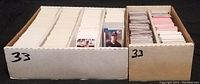 Two cardboard boxes full of trading cards arranged in rows, some cards displayed in front for viewing.