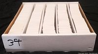 Top view of a large white cardboard box with five vertical sections filled with thick stacks of plain white-backed trading cards.