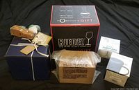 Overall lot view showing boxed Riedel glassware and other packaged gift items on black background.