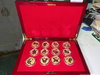 Opened red wooden box holding all 12 zodiac coins in red velvet-lined slots.