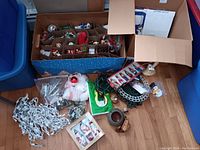 Wide view of assorted Christmas decorations including boxed vintage ornaments, bagged decorations, and coiled string lights on the floor.