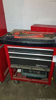 Front view of the red Craftsman tool chest showing the three drawers and lower storage compartment on caster wheels with some hand tools partially visible on top.