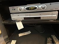 Front view of Sony SLV-D271P DVD/VHS combo player with visible front panel and controls. Remote control placed nearby. Cable box present above but not included.