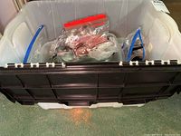 Plastic bins contain multiple spoons, forks, and knives in various sizes and patterns packed in plastic bags or loose inside bins.