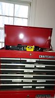 Red Craftsman top and upper drawers with labels for knives, saws, drivers, pliers, screwdrivers, wrenches, drill bits, and rivets.