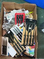 Box containing multiple packs of Tramontina Pulsar II 4-piece steak knife sets in original packaging along with other kitchen gadgets and utensils.