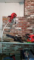 Grasshog trimmer with curved shaft, Remington chainsaw attachment, and Black & Decker hedge trimmer on metal surface against brick wall