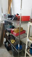 Full view of metal shelf unit showing 5 tiers with various items placed for scale, contents not included in lot