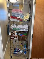Front view of metal rolling shelving unit with towels and household supplies on shelves.