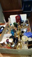 Overview of multiple perfume and aftershave bottles in a cardboard box, several partial bottles including clear, blue, and amber glass containers.