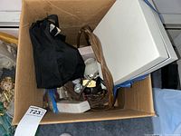 View into cardboard box showing various items including jewelry box, watches, and porcelain pieces.