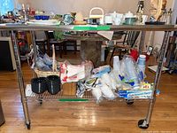 Full view of metal cart with various household items on the top and bottom shelf (items not included in lot).