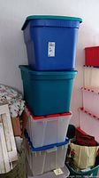 Four stacked plastic storage bins showing blue, teal, and translucent colors with lids