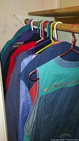 Seven women's outerwear items hanging on a wooden closet rod with plastic hangers, showing colors and styles including denim vest at front.