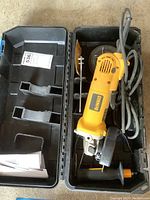 DeWalt yellow small angle grinder in open black plastic case with manuals visible in case compartment