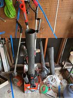Black and Decker electric blower standing upright with tools hanging on pegboard behind it.