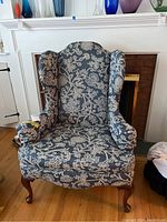 Front view of blue and cream floral upholstered wingback chair showing overall design and condition.