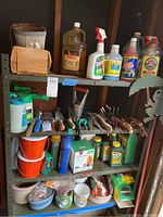 Photo showing four shelves holding assorted garden chemicals in spray bottles, several small ceramic and plastic planters, orange plastic buckets, and a variety of garden hand tools such as pruners and trowels.
