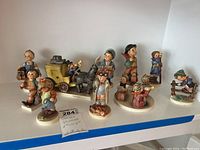 Full view of all ten Goebel Hummel figurines arranged in a group including children and a horse-drawn carriage.