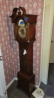 Full view of grandmother clock showing wooden case, rounded top with finial and glass door panels.