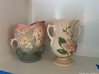 Two Hull Art pottery vases shown side by side with floral decoration and double handles.