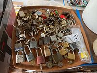 Wide view showing assortment of metal padlocks and a large number of keys spread out on a wooden surface.