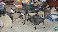 Round black metal mesh patio table with 4 matching black metal mesh chairs on linoleum hex patterned floor. Several baskets on table not included. Signs of wear, scratches and some rust.
