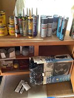 Multiple Minwax wood finish cans, tubes of concrete repair products, and boxed electric fan on a wood shelf.