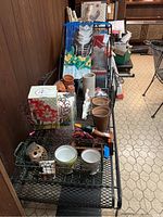 Overview photo showing various terracotta pots, decorative planters, garden flags, and some garden tools on a metal bench.