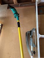 Electric pole chain saw and manual Fiskars telescoping pole saw hung vertically showing overall condition and design.