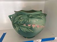 Front view showing the raised bleeding heart floral relief and the soft matte green glaze of the jardeniere pottery piece.