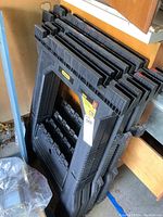 Two pairs of black plastic saw horses stacked side by side in a garage environment showing brand labels and overall condition.