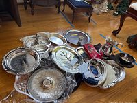 Full view of sixteen-piece silverplate serving set on floor including trays, bowls, pitcher, and utensils.